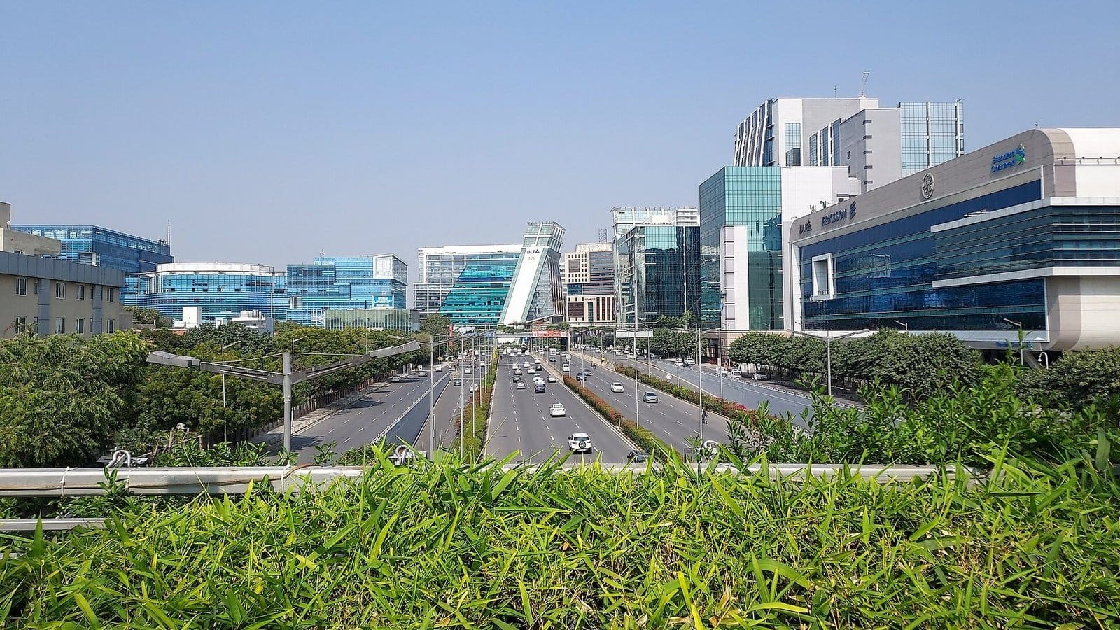 NH-48 running towards the glass office towers of DLF Cyber City, seen over a hedge from a walkway near Belvedere Towers in DLF Phase 2