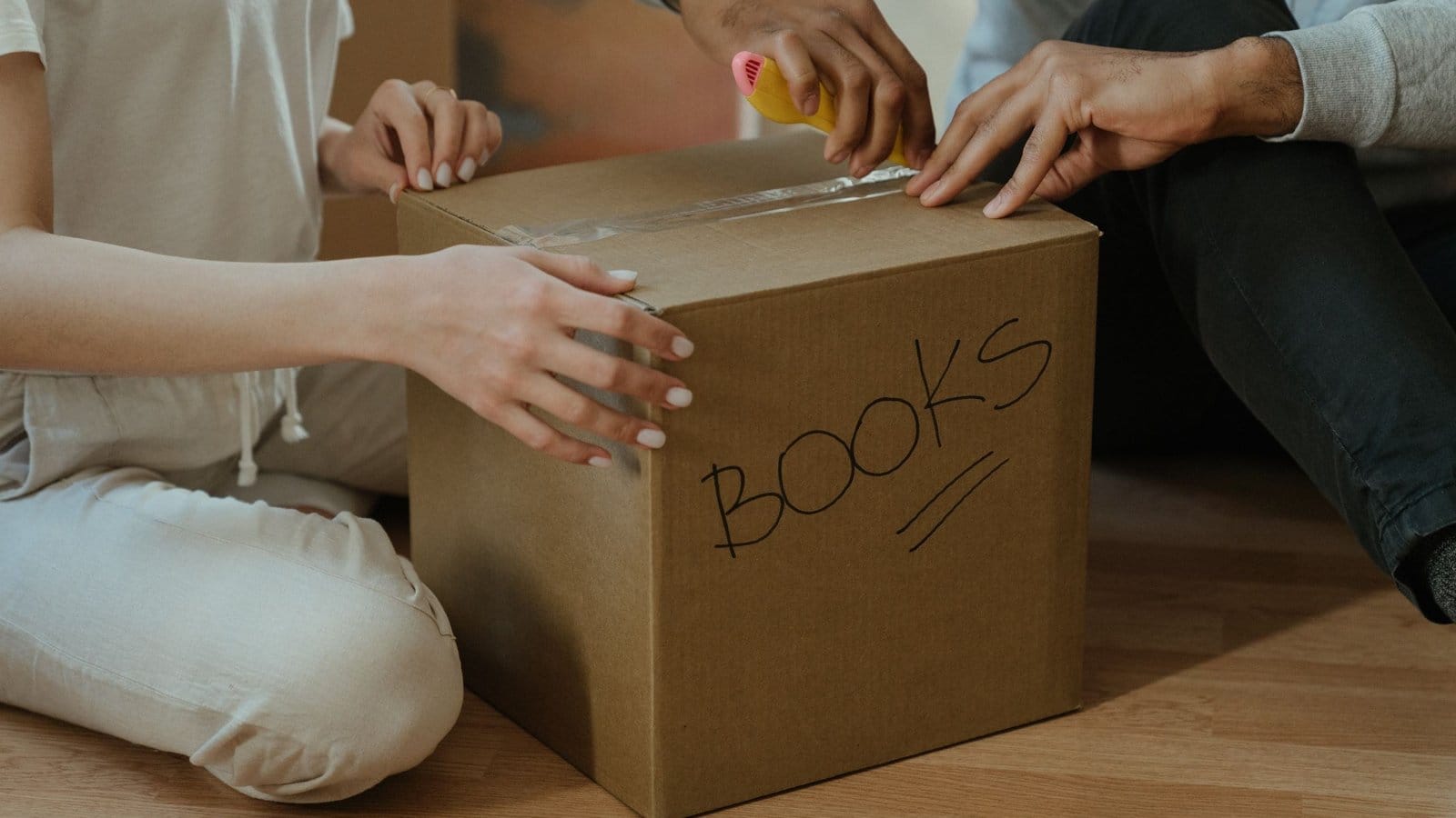 Hands sealing a carton marked BOOKS with tape