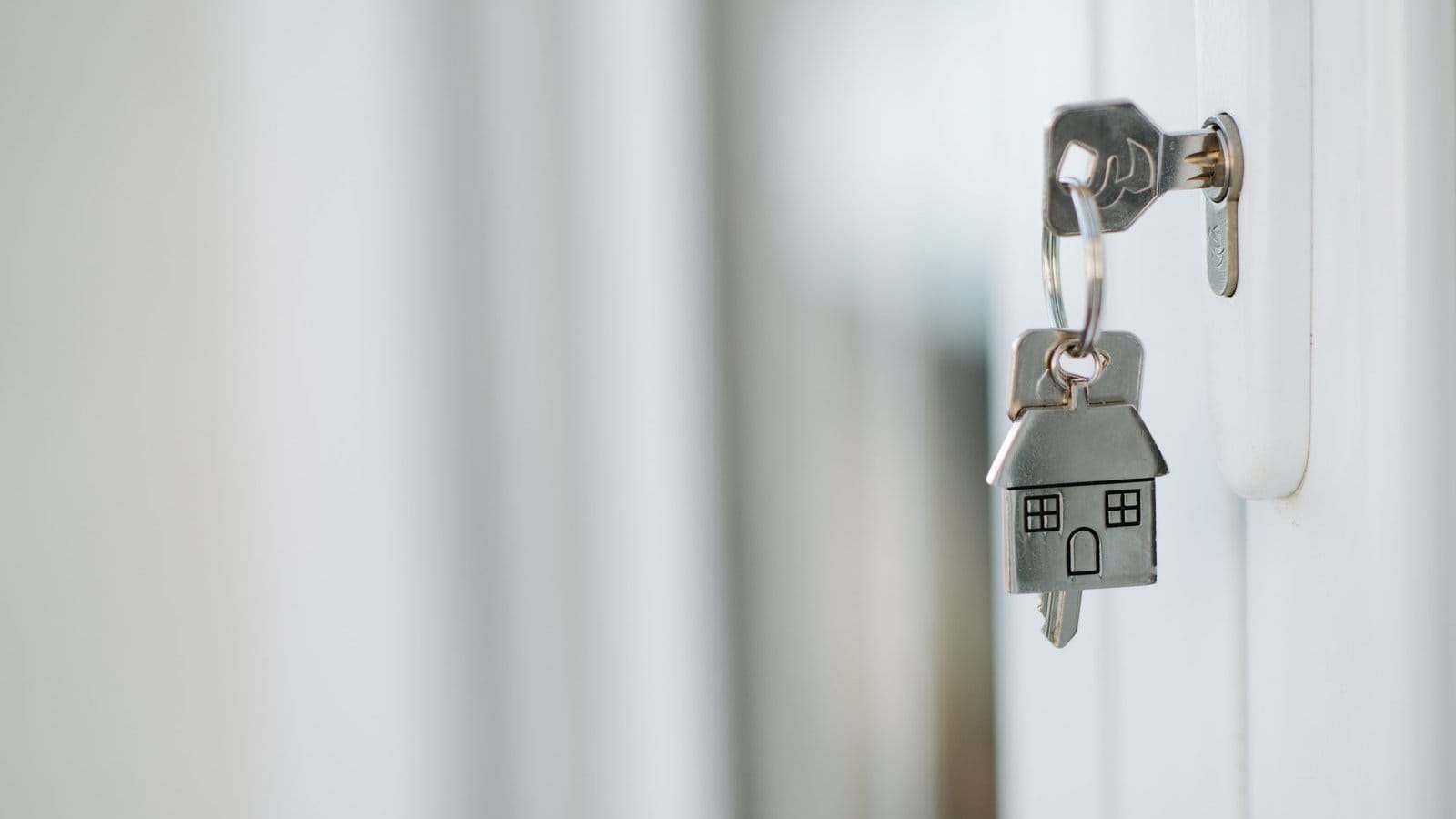 A key with a small house-shaped keychain in a door lock