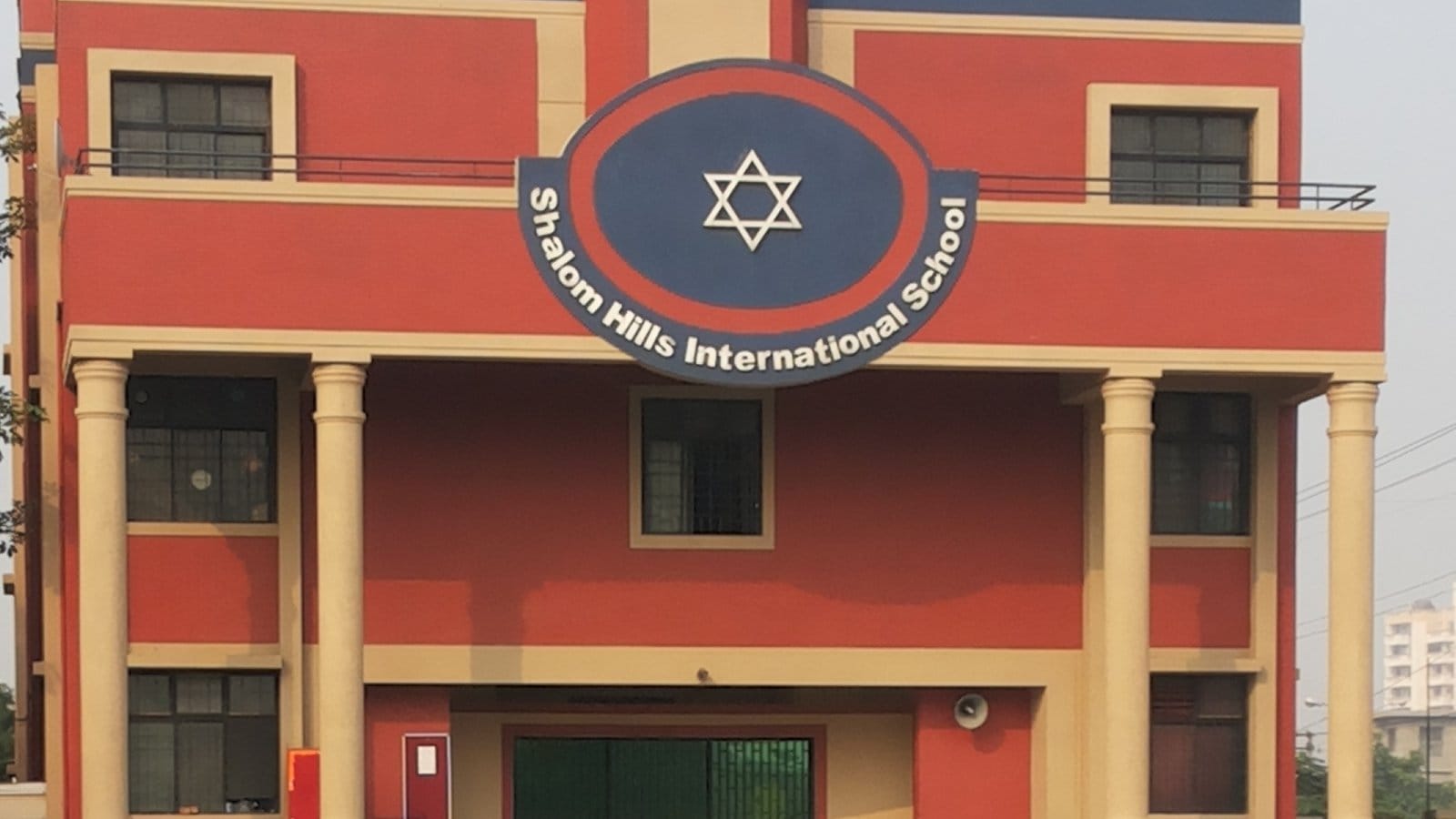 Red and cream front of Shalom Hills International School in C Block, Sushant Lok Phase 1, Gurgaon, with the school's name on a round blue emblem above white columns