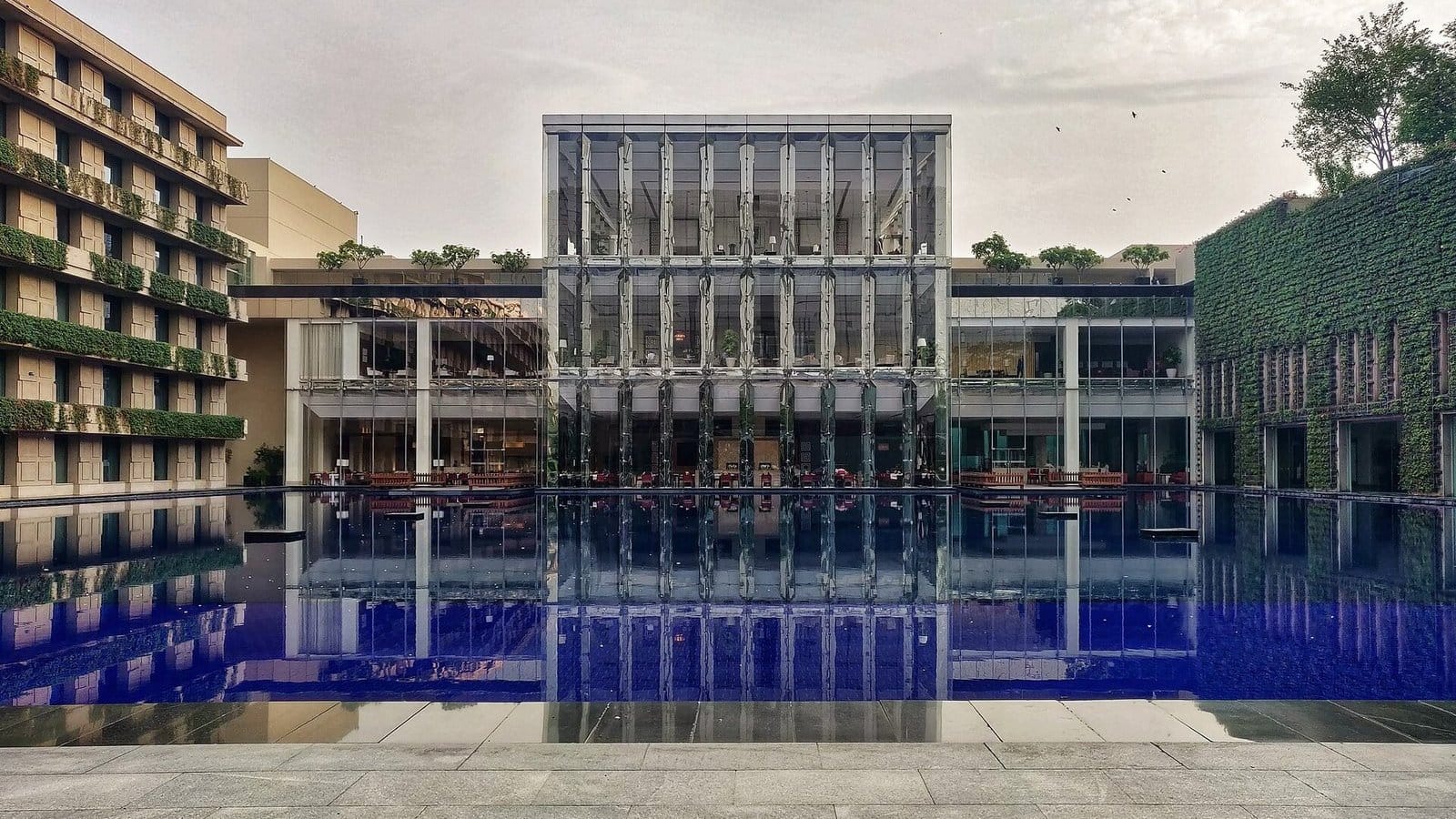 The Oberoi hotel in Udyog Vihar Phase 5, Gurgaon: a glass pavilion reflected in a long blue pool between a planted facade and a green wall