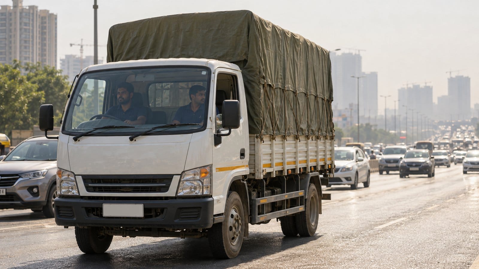 A covered goods truck with two movers in the cab waits in slow traffic on a hot, hazy arterial road