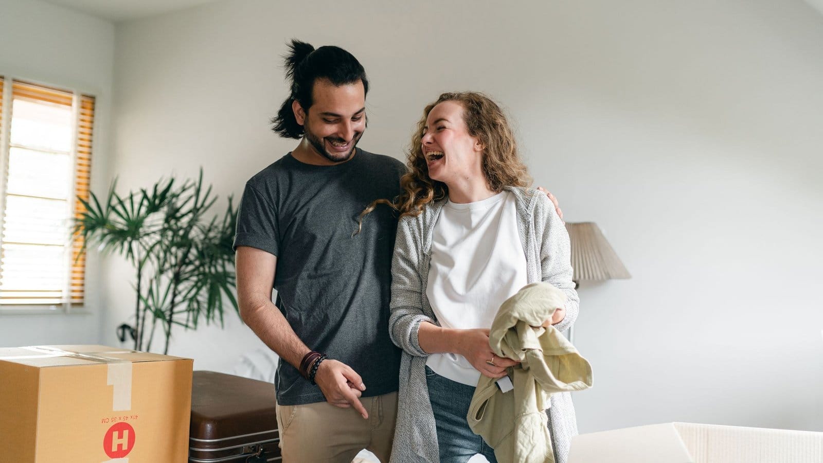 A couple unpacking clothes in a bright new home, a taped carton beside them