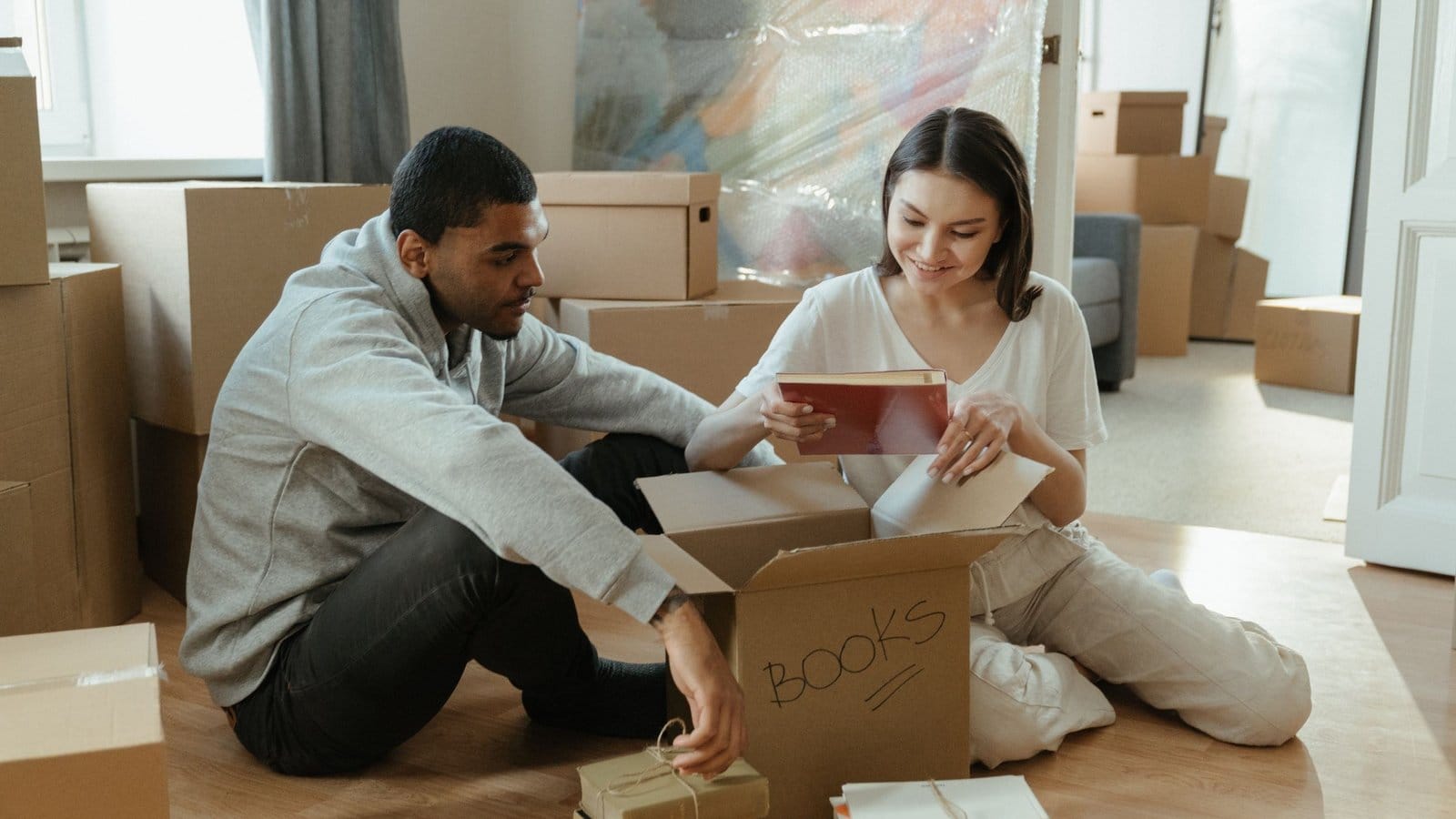 A couple sitting among cartons, unpacking books in a new home