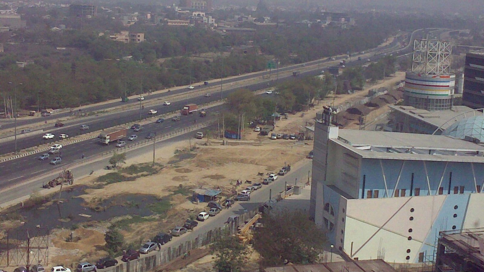 Cars and lorries on the NH-8 expressway, now NH-48, near the 32nd Milestone in Gurgaon, seen from a high floor in April 2009, with open ground and a large building under construction on the right