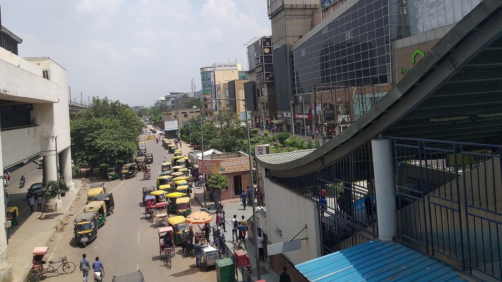 MG Road in Gurugram seen from the MG Road metro station, with auto-rickshaws queued along the kerb below glass-fronted malls