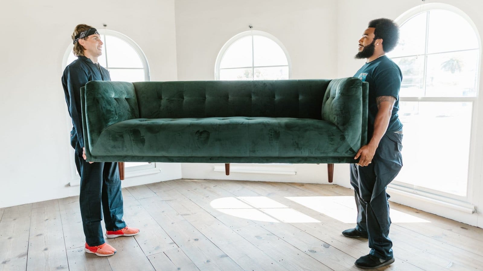 Two men lifting a sofa across an empty room