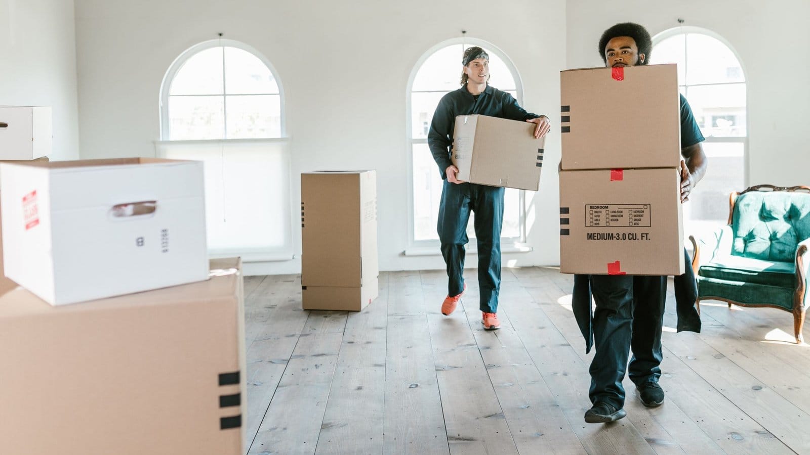 Two men carrying stacked cartons across an empty room on moving day