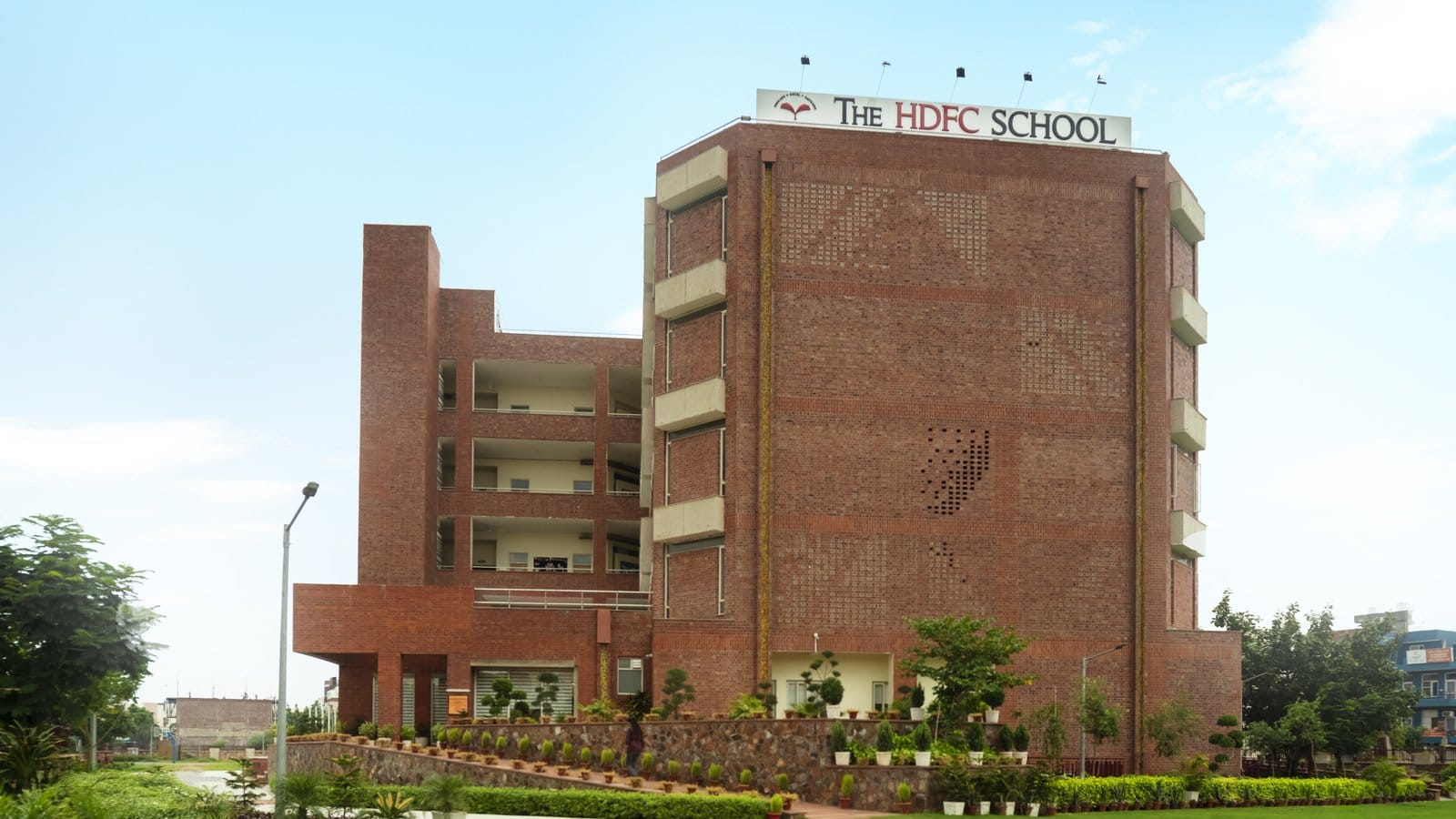 The red-brick senior wing of The HDFC School, now The Knowledge Habitat, in Sushant Lok III, Sector 57, behind a lawn under a blue sky