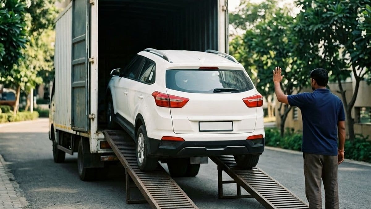 A white SUV backed up two steel ramps into a moving truck on a tree-lined society road while a mover in a navy shirt signals with a raised hand