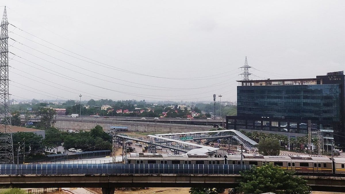 IFFCO Chowk on NH-48 in Gurugram: a Yellow Line metro train on its viaduct, a covered foot bridge over the junction and the glass ABW Tower behind