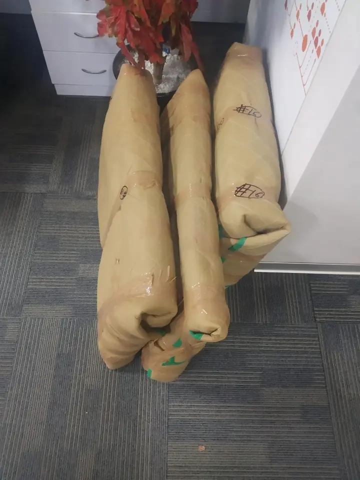 Three items wrapped in brown quilted padding and tape, numbered in marker, standing on an office carpet