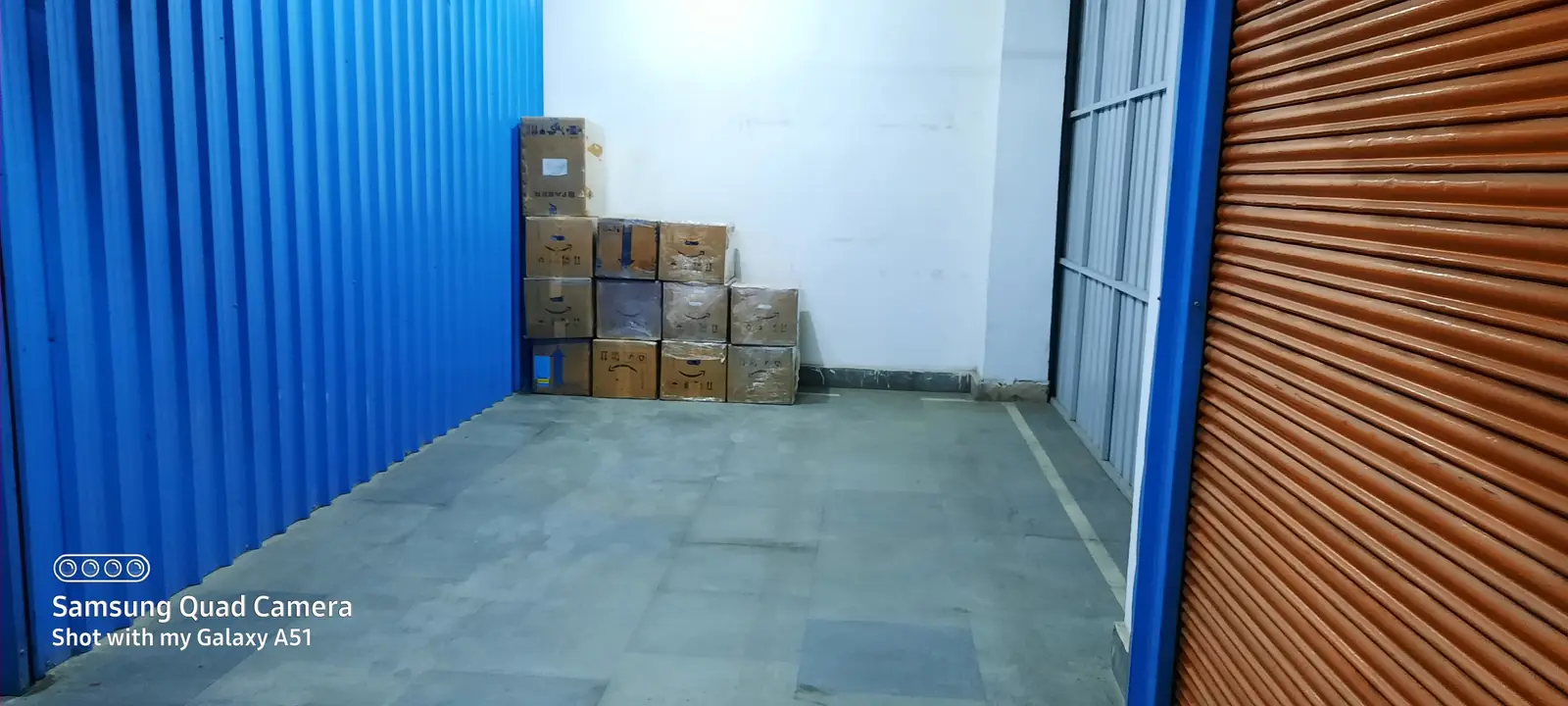 Sealed cartons stacked in one corner of a clean storage unit with blue corrugated walls