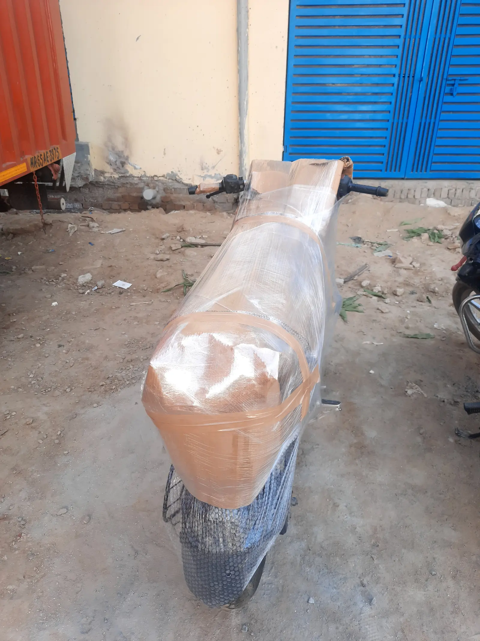 A motorbike wrapped in cardboard, bubble wrap and stretch film, parked next to a container truck