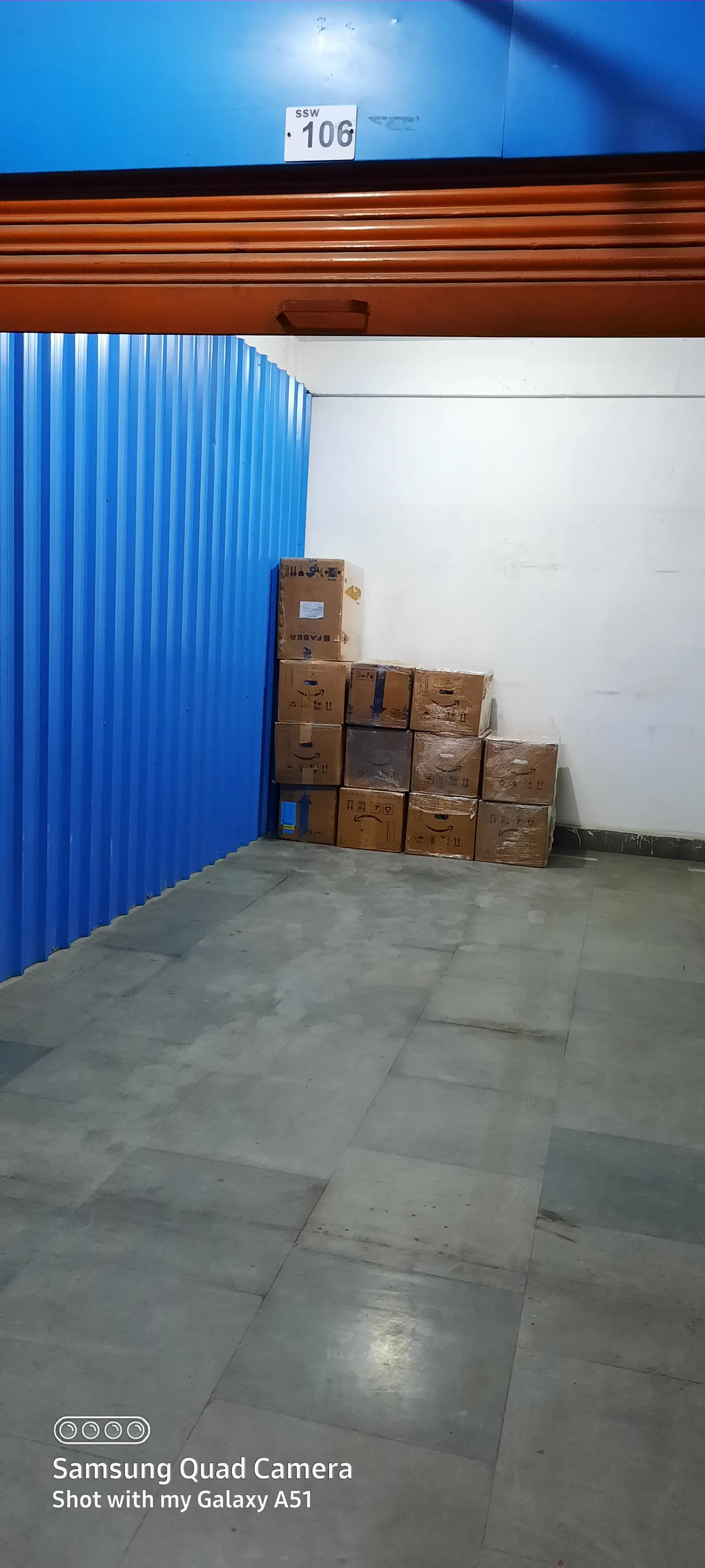 Storage unit numbered 106 with its shutter raised, showing sealed cartons stacked neatly against the back wall