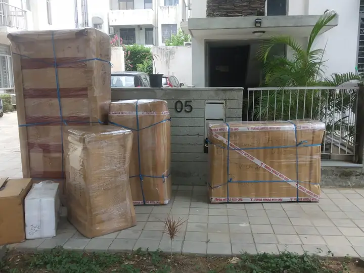 Tall cartons and a TV cabinet wrapped in film, strapped with blue bands and taped FRAGILE, labelled for Pune outside a house