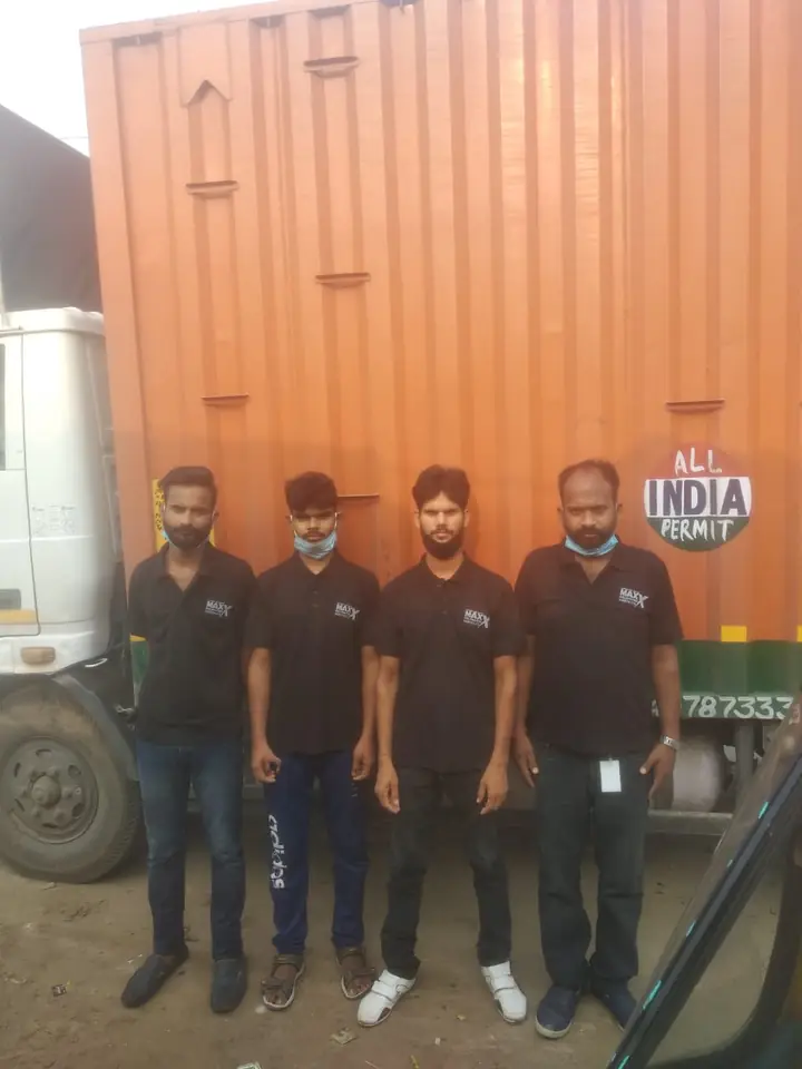 Four crew members in black Maxx Relocation uniforms standing in front of an orange container truck with an All India Permit sign