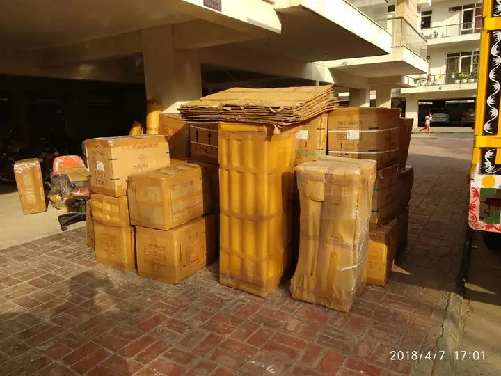 Cartons, film-wrapped furniture and flattened boxes stacked in the parking area under a residential building, photo dated April 2018