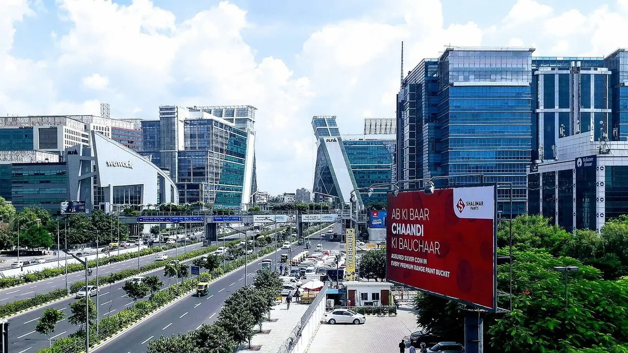 Illustration: dLF Cyber City office towers and the NH-48 approach on a clear day, seen from an overbridge.