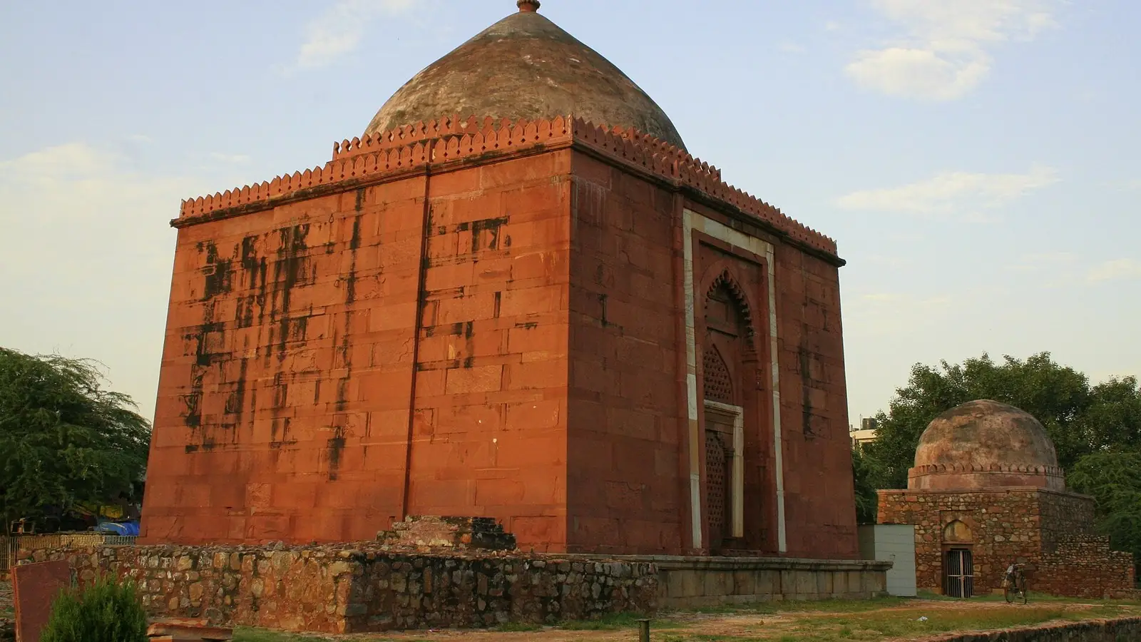 Illustration: lal Gumbad, a red sandstone Tughlaq-era tomb in Malviya Nagar, under a blue sky.